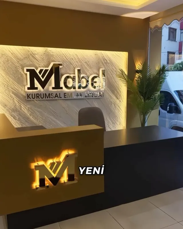 Mabel Kurumsal Emlak ofisinde duvardaki ışıklı logo ve karşılama bankosundaki altın ışıklı M harfi